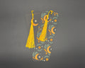 Celestial paper bookmark with rounded corners and yellow fabric tassel. Design shows green and yellow foliage, yellow moons and white stars. 
