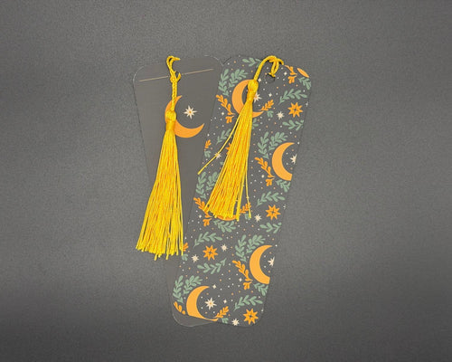 Celestial paper bookmark with rounded corners and yellow fabric tassel. Design shows green and yellow foliage, yellow moons and white stars. 