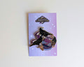 A gothic-themed crow enamel pin from the 'Corvid Collection' displayed on its lavender backing card against a plain white background.