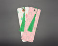 Pink paper bookmark with green and white Christmas wreaths pattern, rounded corners and a green, fabric tassel. 