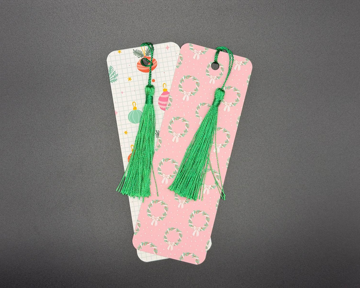 Pink paper bookmark with green and white Christmas wreaths pattern, rounded corners and a green, fabric tassel. 