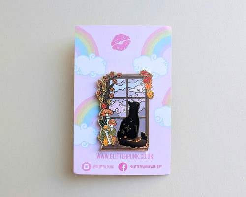 A decorative enamel pin featuring a black cat sitting by a window with flowers and mushrooms, mounted on a pastel pink backing card with rainbows and clouds. The card shows the brand name Glitter Punk.