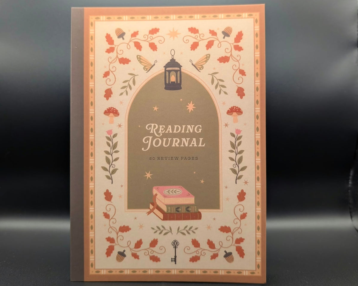 A decorative reading journal with a warm autumn-themed cover illustration, featuring the title 'READING JOURNAL' in a central arch with leaves, stars, a lantern, and stacked books.